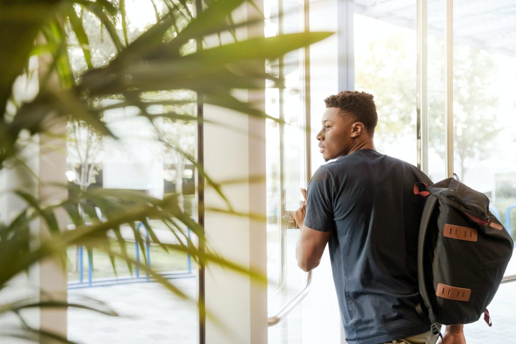 Estudante do curso técnico, ou de graduação, com mochila nas costas saindo da sua Instituição de Ensino.
